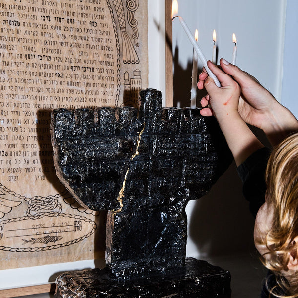 Person lighting candles on a black Menorah with a Ketuba in the background